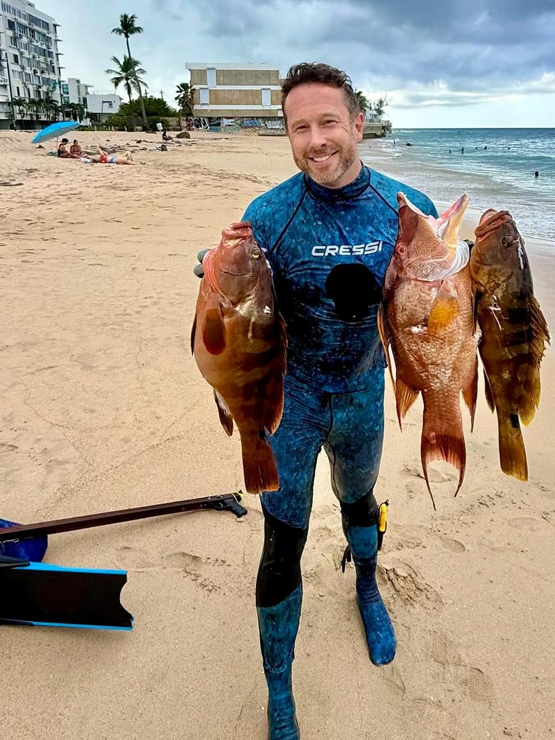 Patrick Horsman in a Cressi wetsuit on the beach in Puerto Rico after a spearfishing dive, holding several reef fish